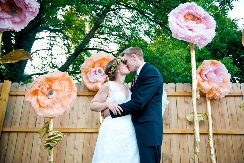 newlyweds kiss in front of large faux flowers
