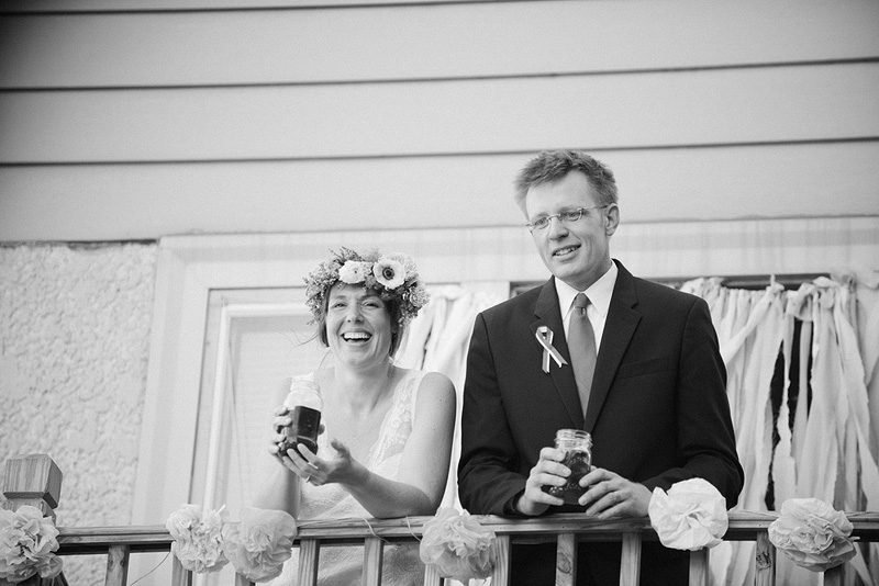 bride and groom look over backyard wedding reception from balcony