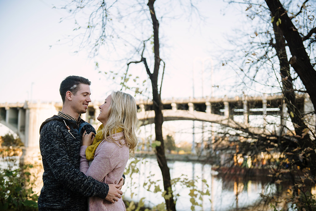 engaged couple embracing beside mississippi river in minneapolis