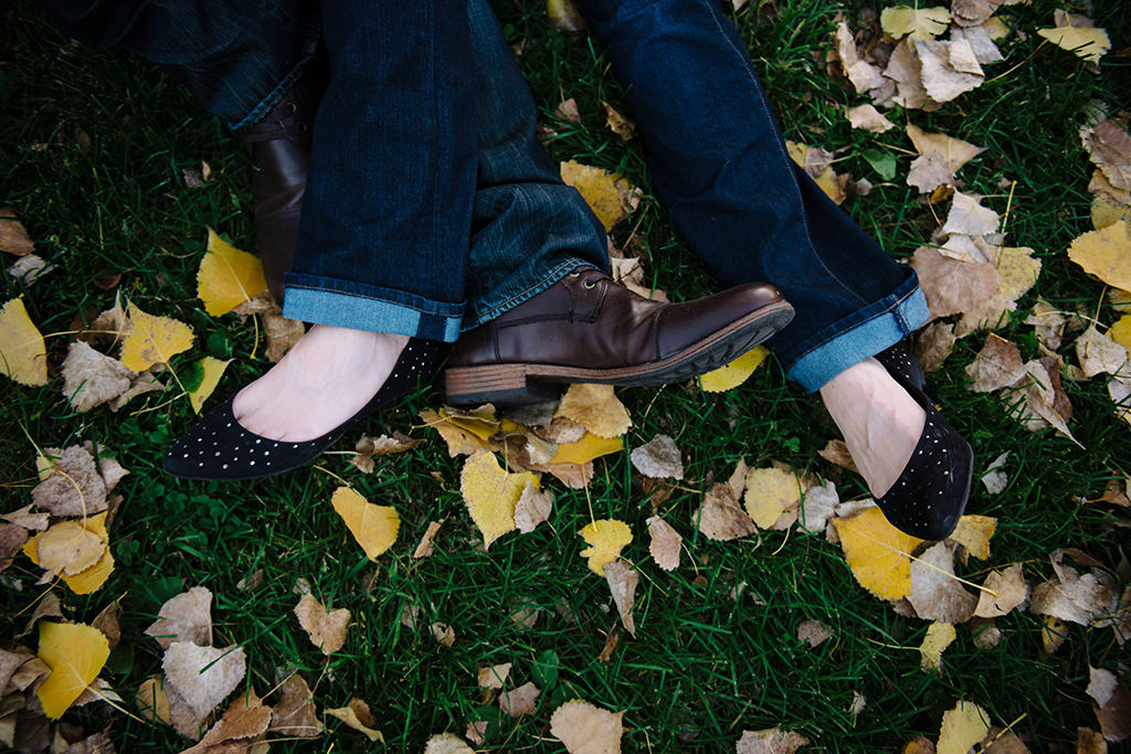 engaged couple entangled feet in grass and fall leaves