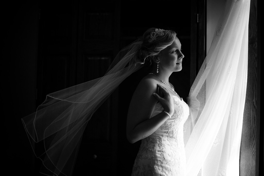 bride in front of window with veil blowing