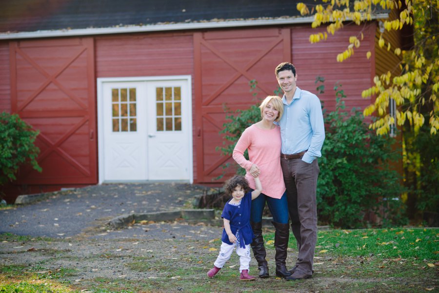 family smiling in front of barn in twin cities