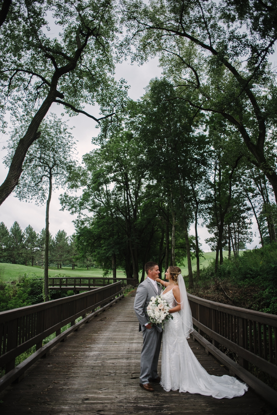 bride and groom looking at one another on bridge with trees in background