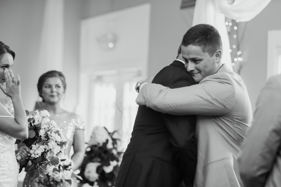 father of bride hugging groom while bride looks on