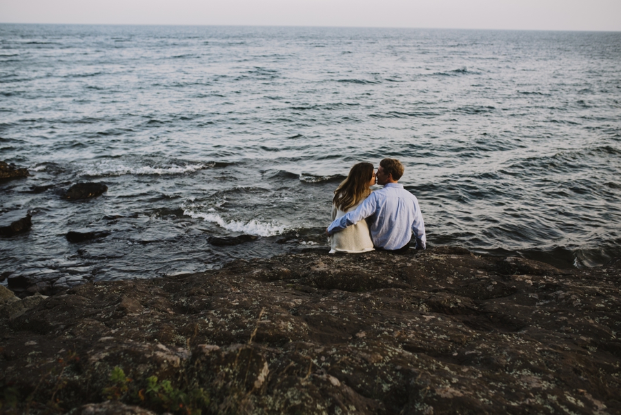 engaged couple kissing beside lake waves