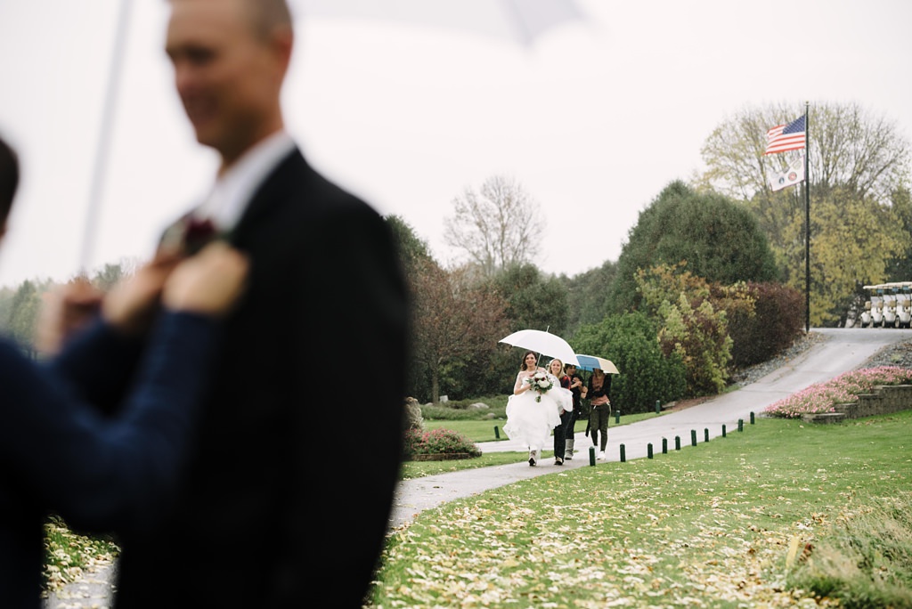 Bride walking up to groom in umbrellas before their first look