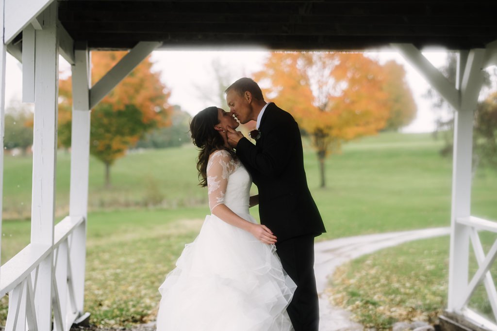 bride and groom kiss under bridge at their farm wedding