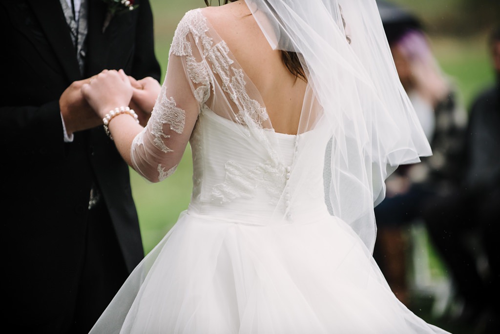 Detail of bride and groom holding hands during wedding ceremony outdoors