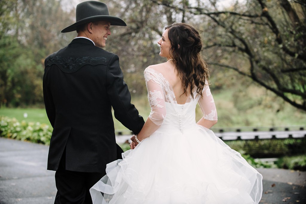 bride and groom with cowboy hat walking away in bliss