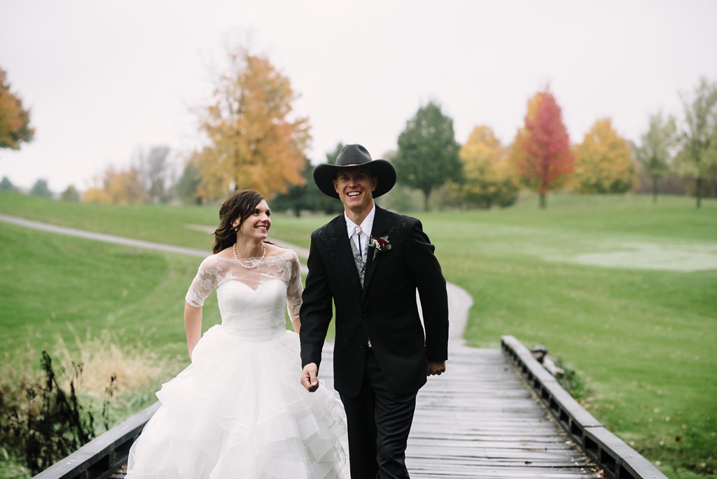 bride and groom walking on a bridge with fall colors in the background