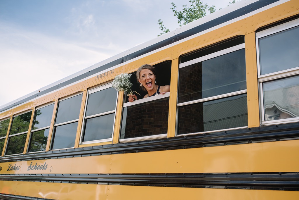 Bridesmaid celebrating outside of school bus during MN wedding