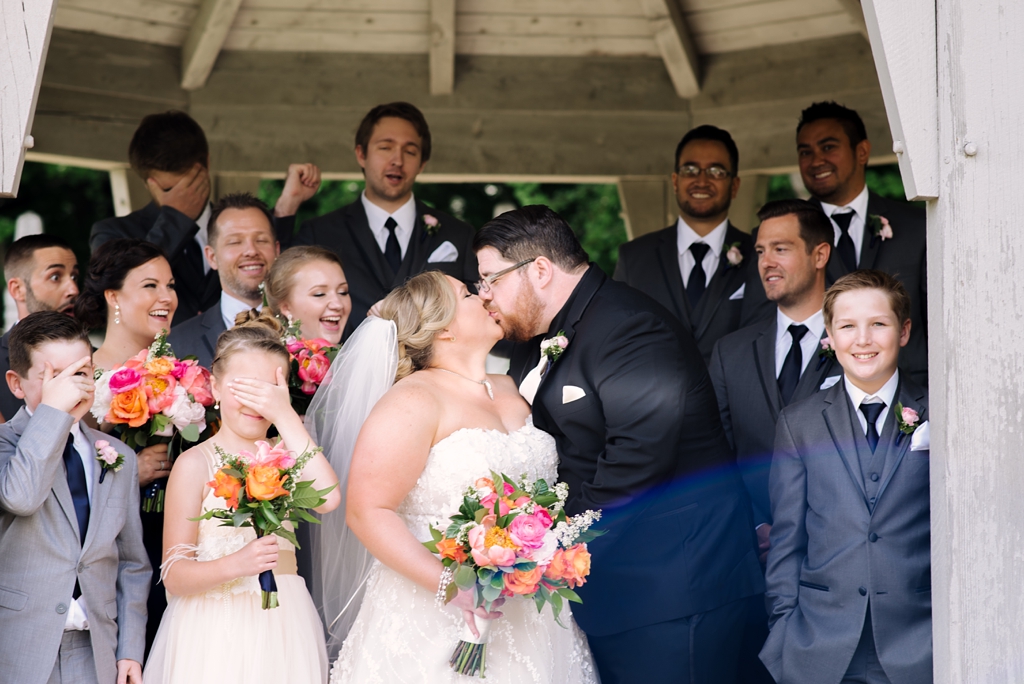 bride and groom kiss surrounded by wedding party