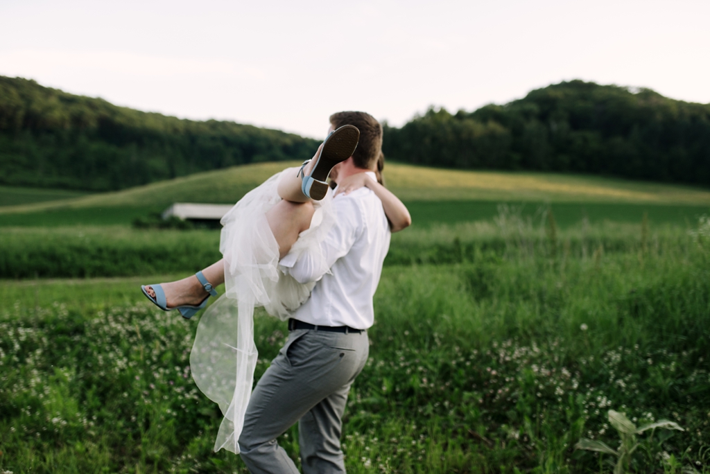 groom lifting bride off feet in green field