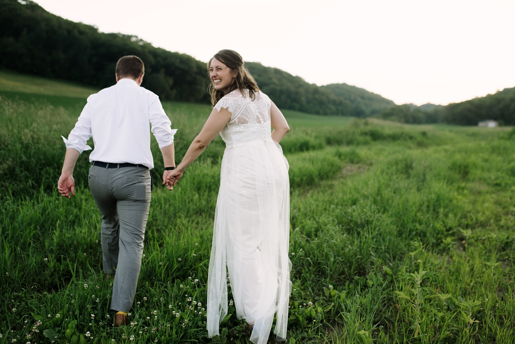 bride laughing while walking through field with groom