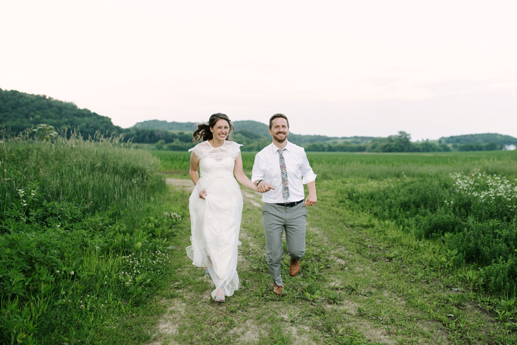 newlyweds running toward camera in wisconsin field