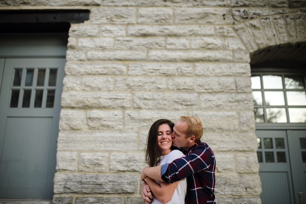 husband kissing wife in front of brown brick building minneapolis