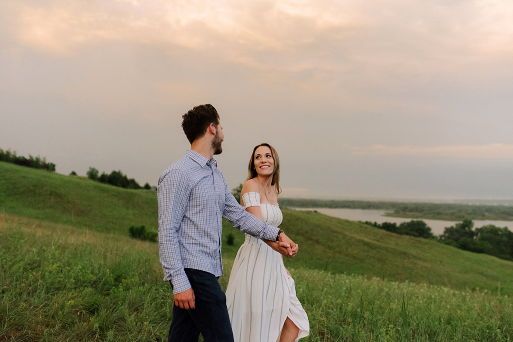 engaged couple holding hands in field at sunset