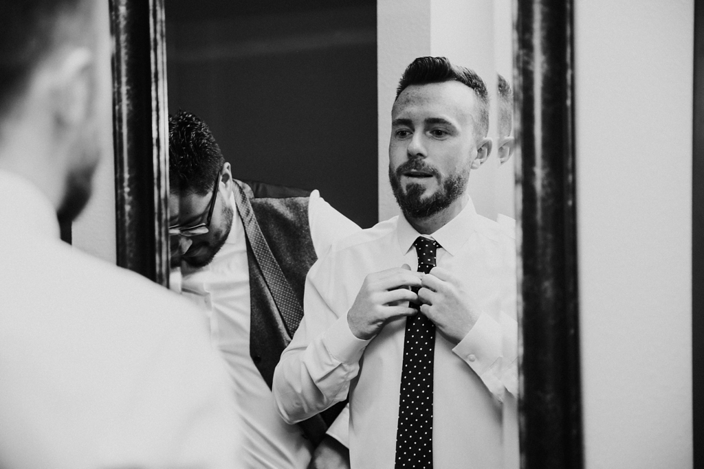 black and white image fixing tie in mirror before wedding