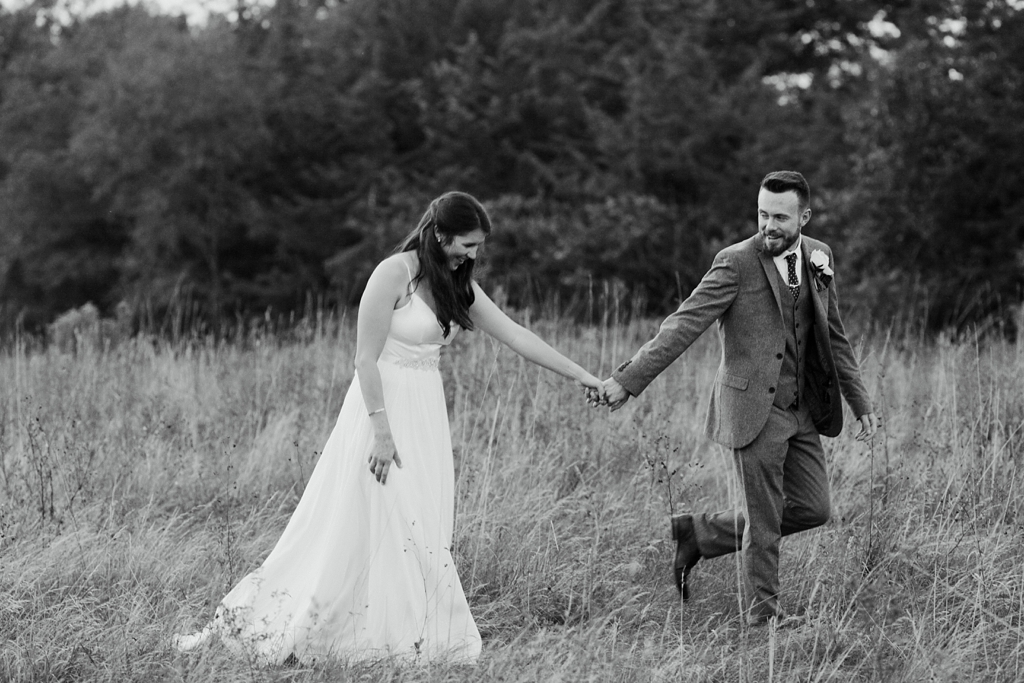 bride and groom walking through field holding hands