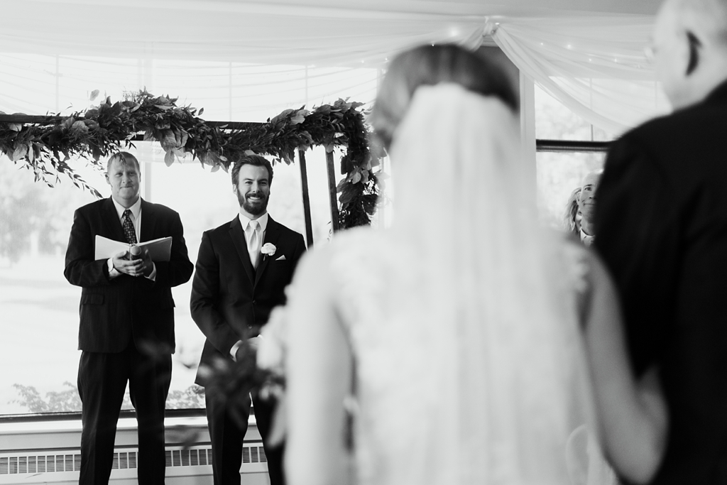 groom smiles at bride walking down aisle
