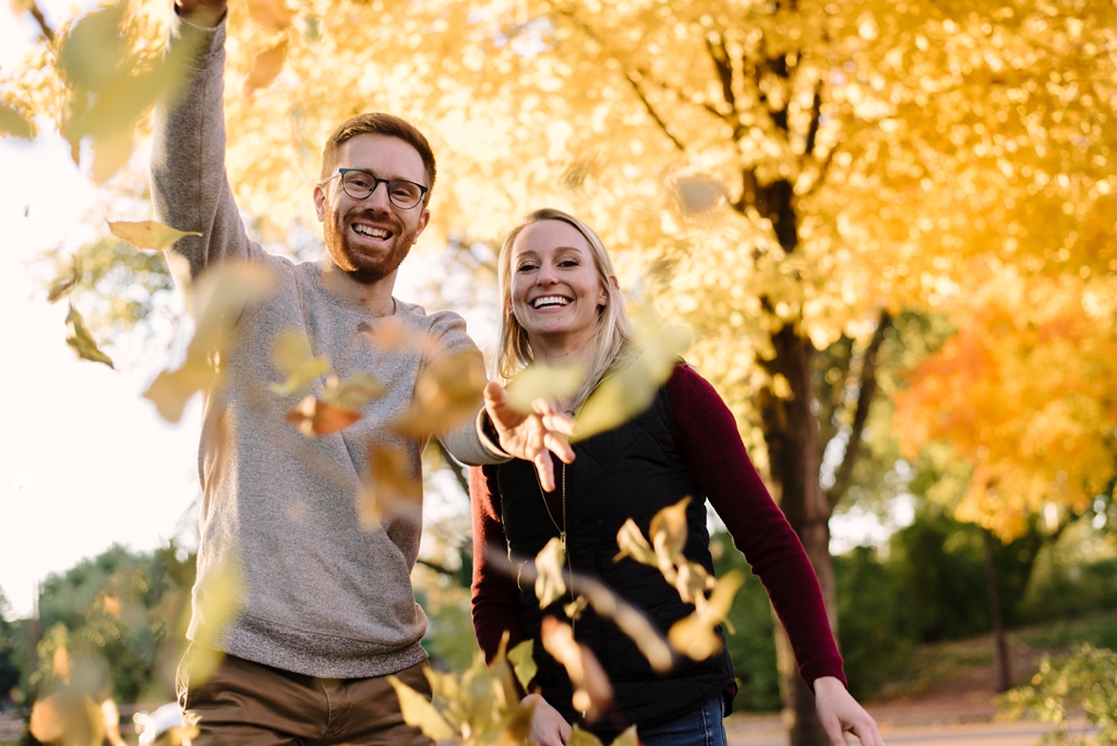 engaged couple throwing fall leaves at camera