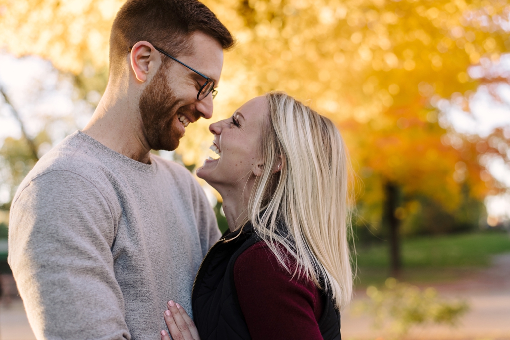 engaged couple laughing in front of fall tree