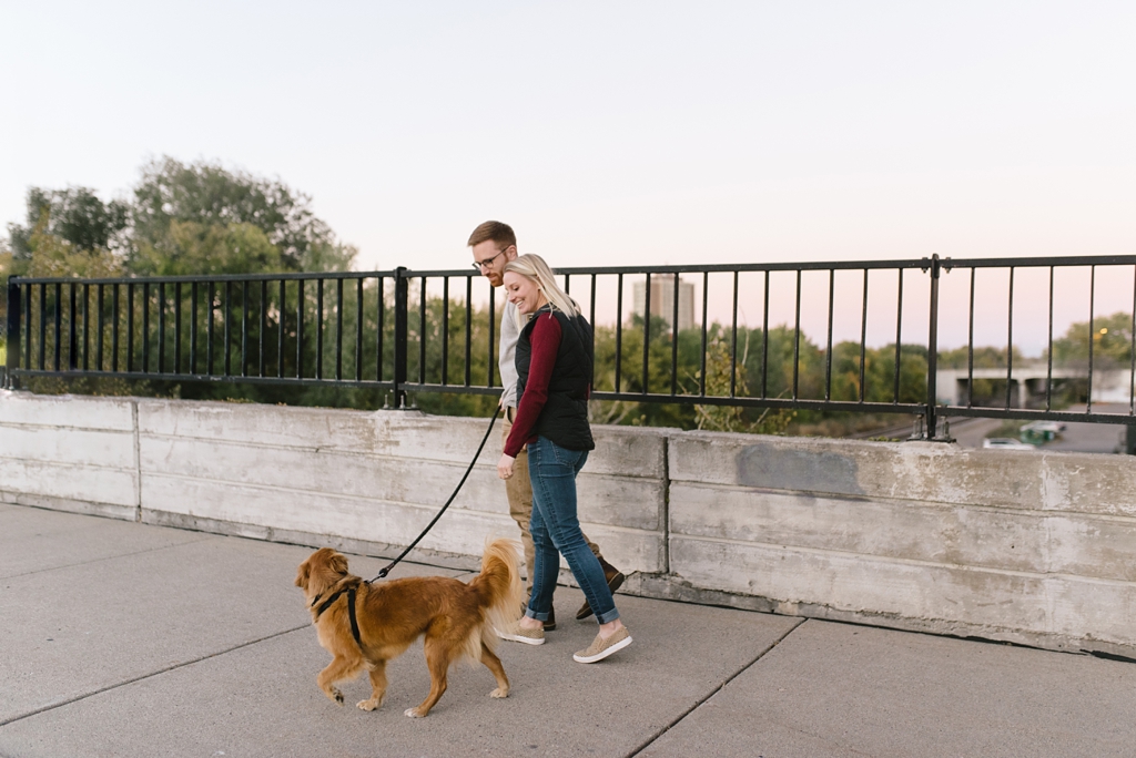 engaged couple walking dog across bridge