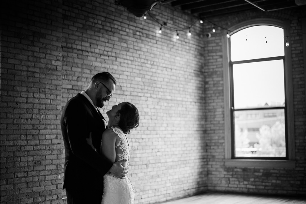black and white image of bride and groom embracing in front of brick wall