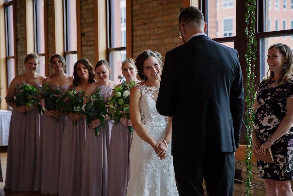 bride smiling at groom during vows with bridesmaids behind