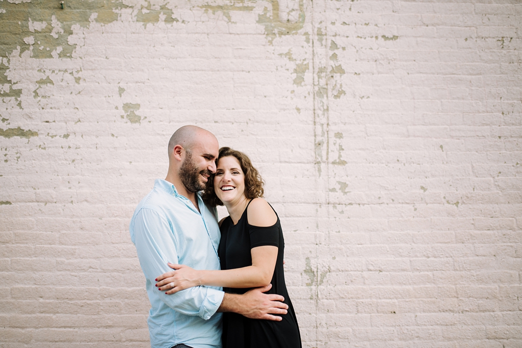 man and woman embrace in front of painted brick wall