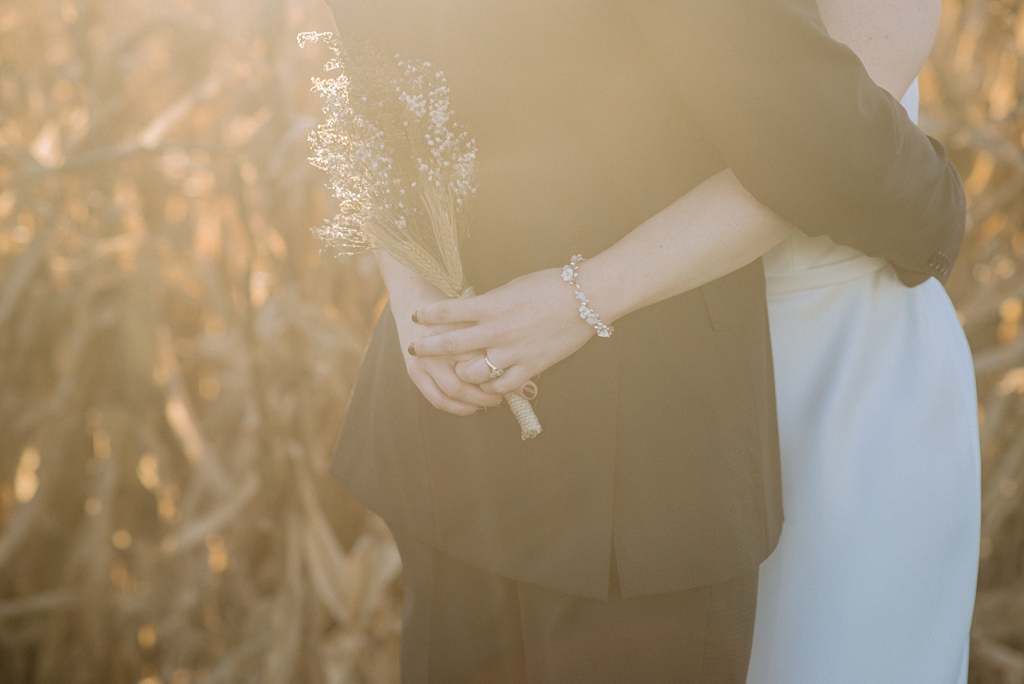 newlywed couple embraces beside corn field at sunset