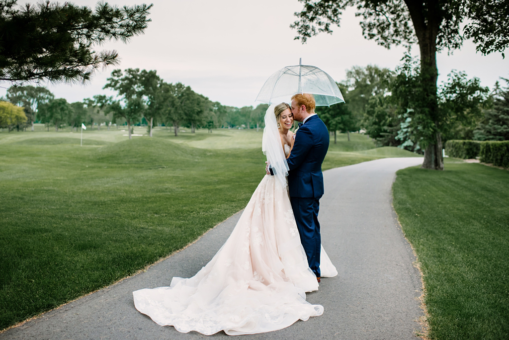 newlyweds pose on golf course with clear umbrella