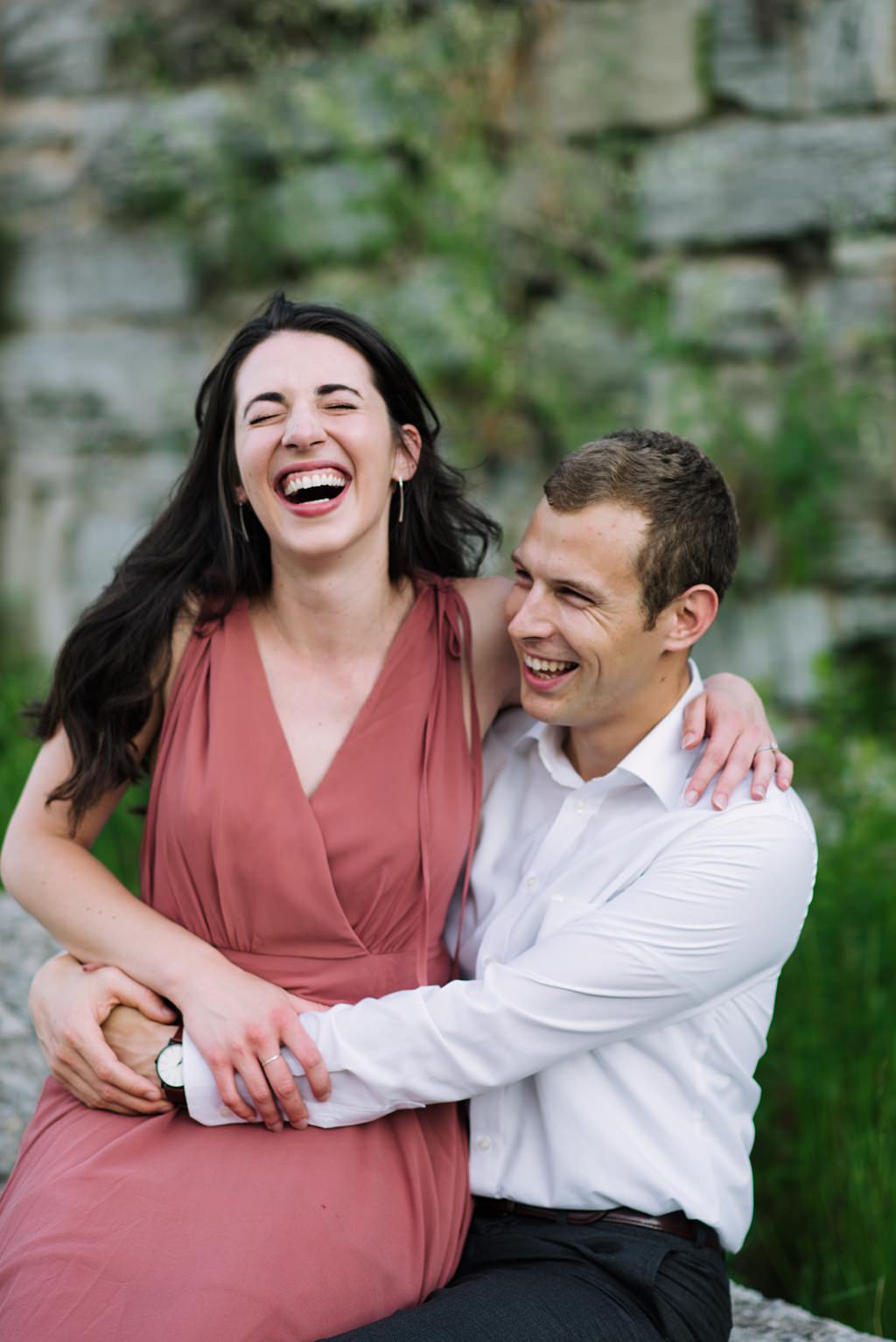 couple laughing in front of stone wall with greenery