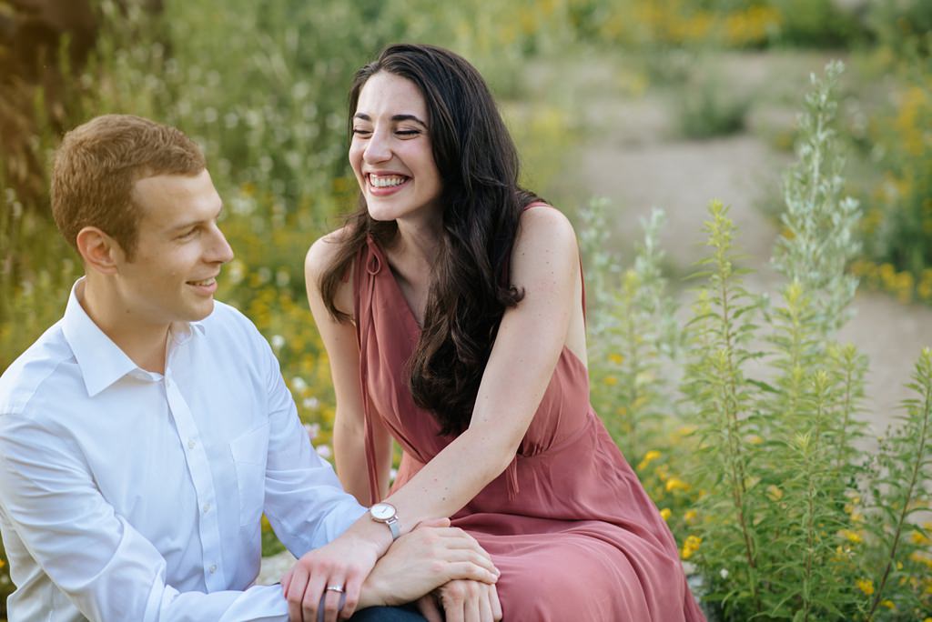 laughing engaged couple sitting in field of green