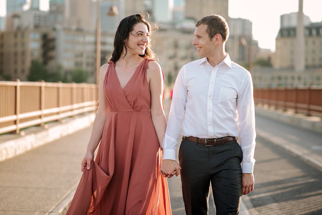couple smiling at one another as they walk down stone arch bridge