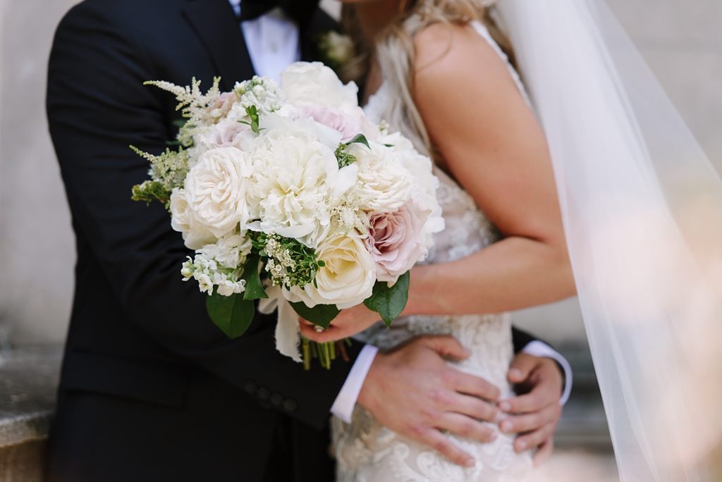 detail of wedding bouquet while bride and groom embrace