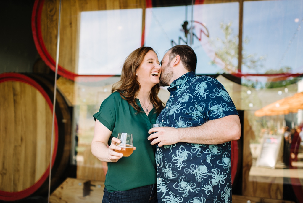 couple laughing with cup sin hand during their brewery engagement session
