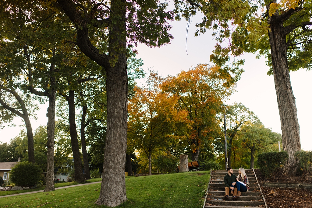 couple sitting on steps outside beneath trees with fall foliage