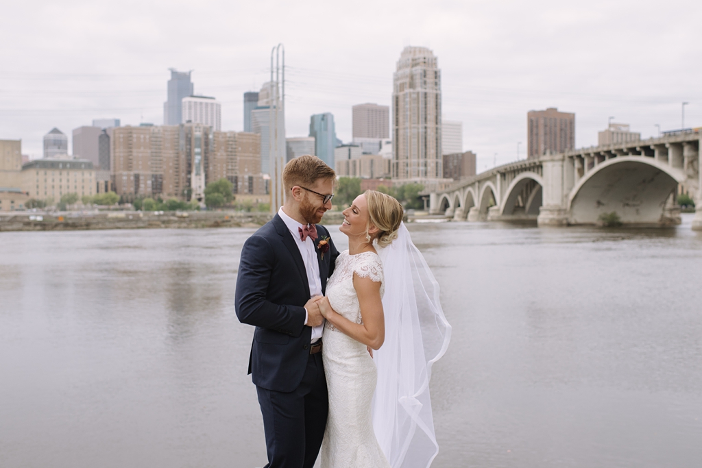 bride and groom smile at each other and hold hands beside mississippi river