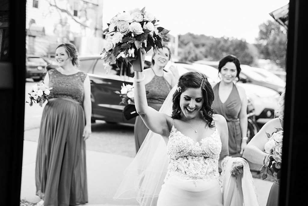 bride walking with bridesmaids and raising bouquet in the air