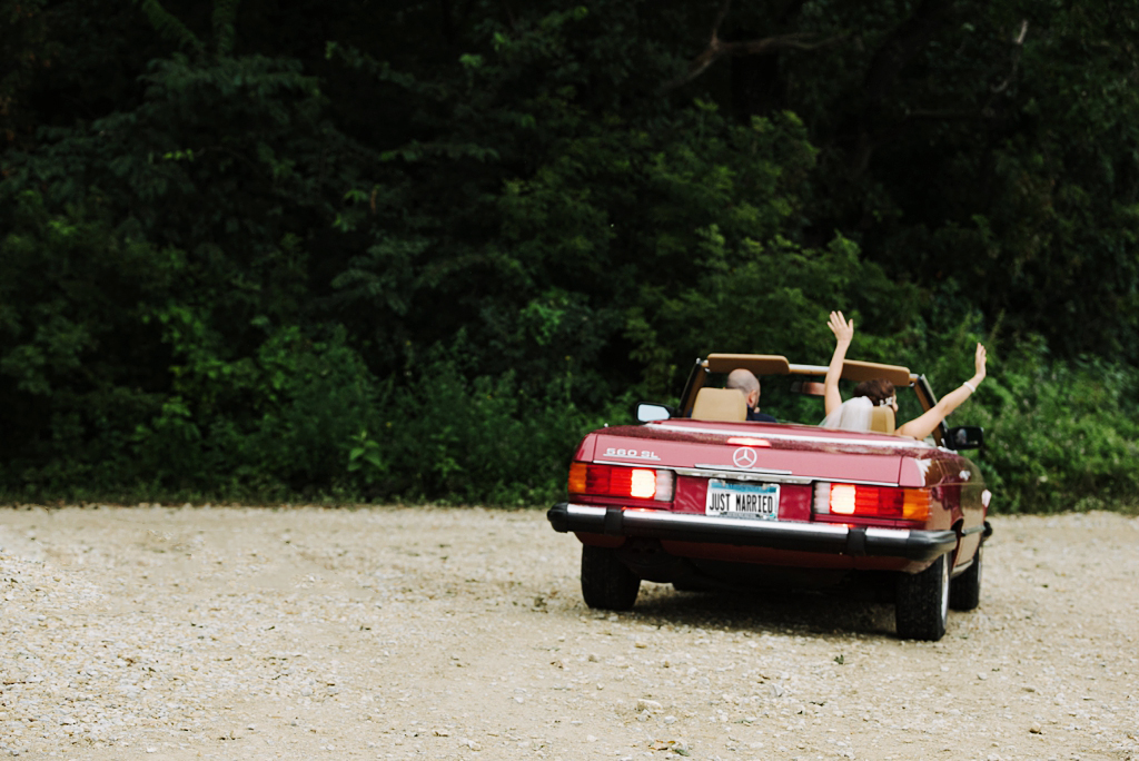 bride and groom in convertible with just married license plate