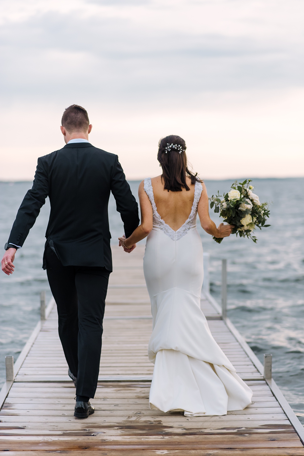 bride and groom walk away down wet dock onto lake