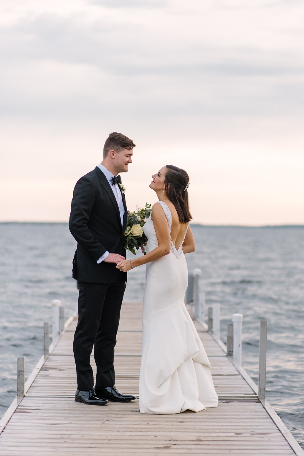 bride and groom smile at each other on lake dock