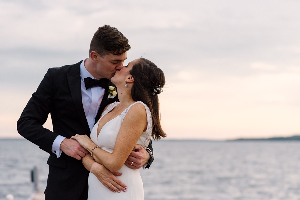 newlyweds kiss on lakeside dock at sunset