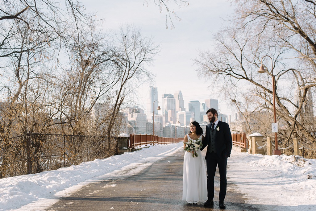 winter newlyweds walk with minneapolis skyline