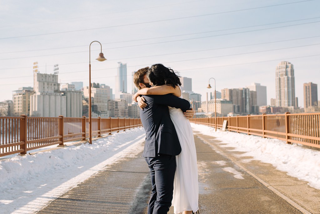 bride and groom embrace on snowy stone arch bridge