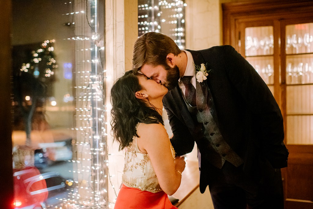 newlyweds kiss in front of window with twinkle lights at 4bells