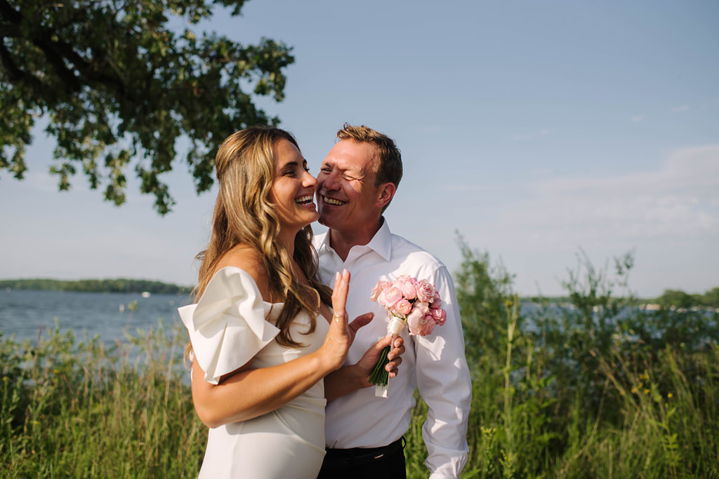 bride and groom laugh beside lake before elopement