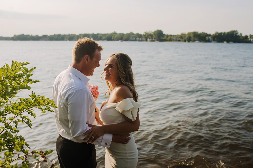 bride and groom smile beside lake minnetonka