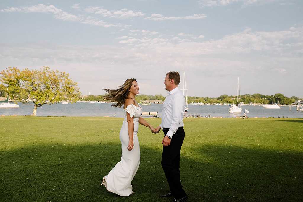 bride and groom dance in grass beside lake